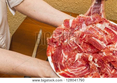 person, cut ham,person serving a plate of jamon,person working