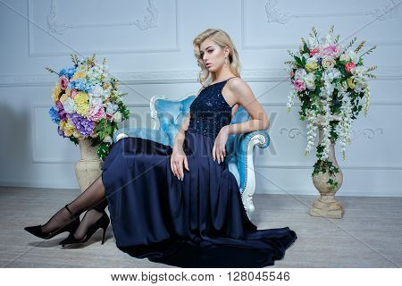 Young beautiful blond woman in dark blue dress posing at white studio
