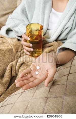 Kavkazská/Hispanic mladá žena v ruce drží prášky se sklenicí vody.