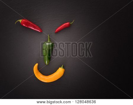 Face made from different chili peppers on black stone
