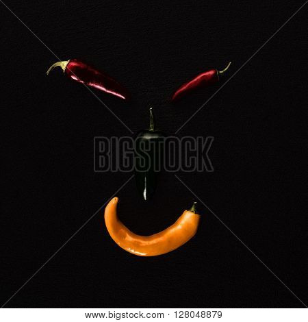 Face made from different chili peppers on black stone, low key
