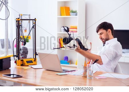 Fire away.  Pleasant cheerful handsome man holding model printed on 3d printer and sitting at the table while feeling gladness