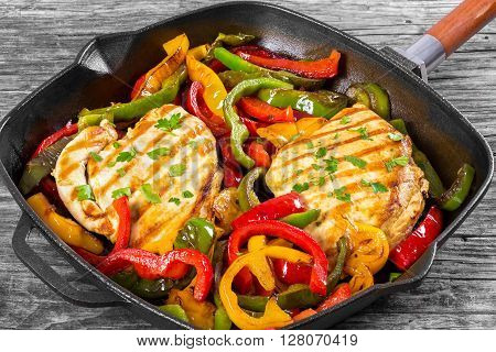 Delicious Grilled Chicken breast fillet and fried bell pepper on a skillet on an old rustic table horizontal close-up