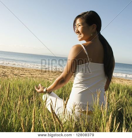Young Asian femmes assis sur la plage de méditer et regardant au large sur le côté.