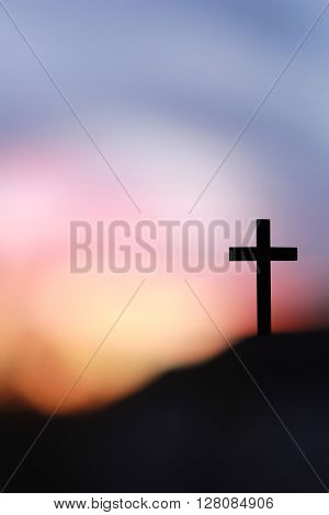 The Cross of Jesus Christ on the rock against blurry sunrise
