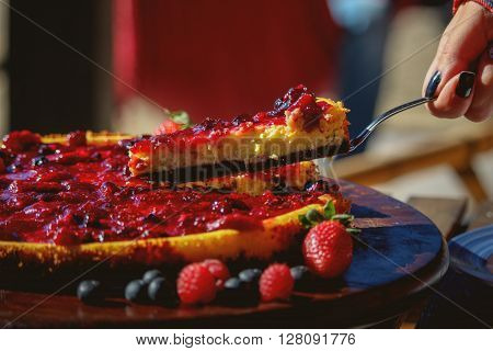 Piece of berry fruits cheesecake on wood plate with strawberries, blueberries and raspberries