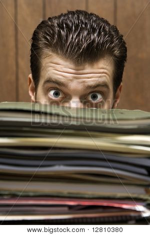 Lüneburg Mid retro Geschäftsmann peering mit großen Augen, die über einen hohen Stapel von Ordnern.