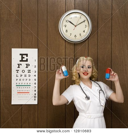 Caucasian mid-adult female nurse standing by wood paneling holding oversized pills and smiling at viewer.