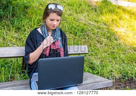 Young woman using laptop at a riverbank. Milleanial working in a park.