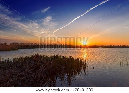 Sunset over a swamp lake aircraft trail in the sky.