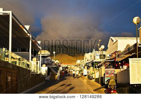 TENERIFE ISLAND, SPAIN - OCTOBER 28, 2015 : Alley near the sea with small shops and restaurants in the rays of the setting sun in Costa Adeje, Canary Islands