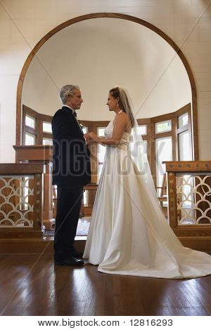 Protrait til bruden og gommen holder hinanden i hænderne på alteret i en kirke.