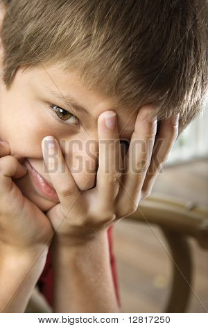 Portrét kavkazské pre-teen chlapce s rukou částečně přes tvář.