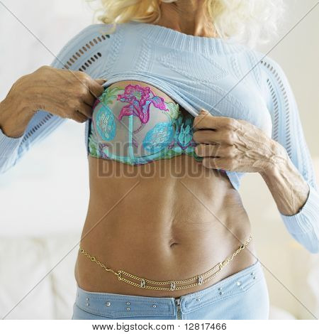 Tan Caucasion หญิงวัยกลางคนยกเสื้อของเธอเปิดเผย midriff และเต้านมของเธอดึงดูดใจ