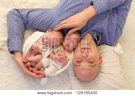 Father lying on a flokati holding his identical twin babies of 3 weeks old