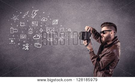 An elegant hipster guy trying to use a vintage camera with camera settings icons drawn on wall, like flash, white balace or ISO value concept