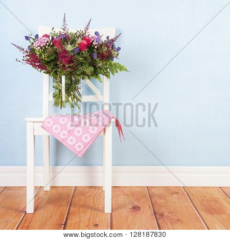 Chair with vase mixed bouquet flowers on blue background