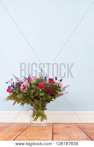 Glass vase mixed bouquet flowers on floor in room with blue background