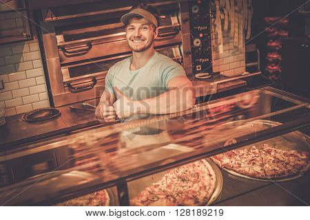 Handsome pizzaiolo standing at kitchen in pizzeria.