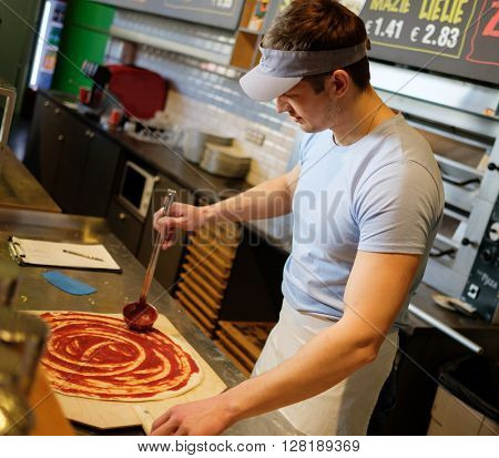 Handsome pizzaiolo making pizza at kitchen in pizzeria.