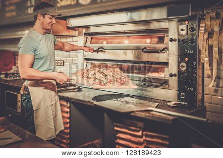 Handsome pizzaiolo making pizza at kitchen in pizzeria.