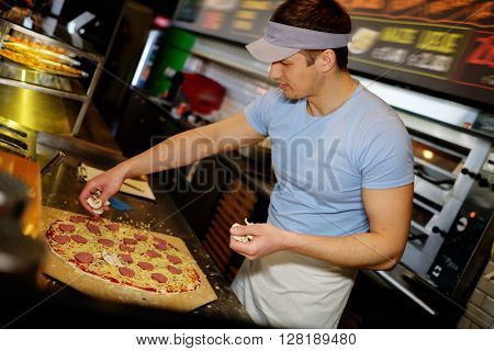 Handsome pizzaiolo making pizza at kitchen in pizzeria.
