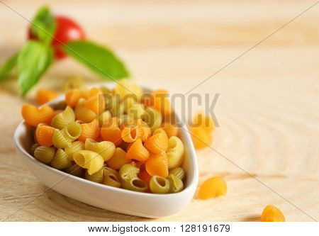 Dry multicolored gomiti pasta in white bowl on wooden table