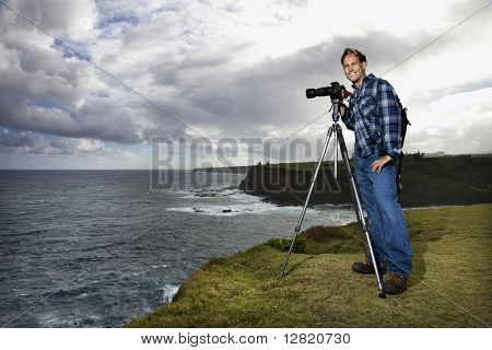 Pie hombre mid-adult caucásico con cámara en trípode mirando el visor en el acantilado de la o