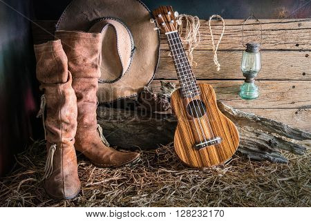 Still life painting photography with ukulele on american west rodeo brown felt cowboy hat and traditional leather boots in vintage ranch barn background