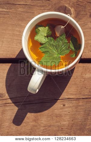 Top view of tea with currant leaf in white cup