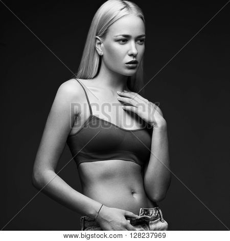 sexy fashion model with long hair, young European attractive, beautiful eyes, full lips, perfect skin is posing in studio for glamour vogue test photo shoot showing different poses. Picture taken in the studio on a gray background. Black and white photo