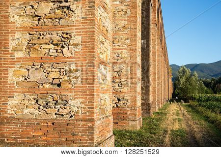 Ancient Aqueduct and Footpath - Section of the Nottolini Aqueduct in Tuscany near Lucca Italy. Warm evening light with classic Tuscan textures and tones. Footpath in right frame with distant person for scale.