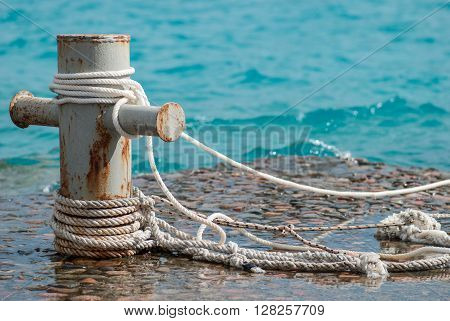 Rusty mooring bollard with ship ropes and  clear turquouse sea ocen water on background.