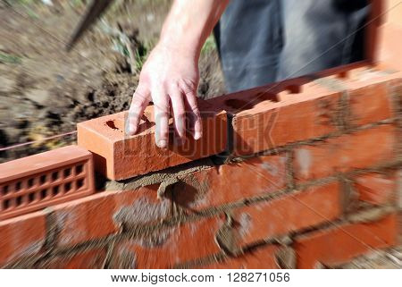 Closeup of bricklayer during the building of a house extension. Zoom effect applied centered on hand holding brick.