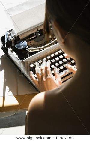 Pohled zezadu na nahé mladé asijské ženy sedí u kuchyňského stolu, psaní na stroji.