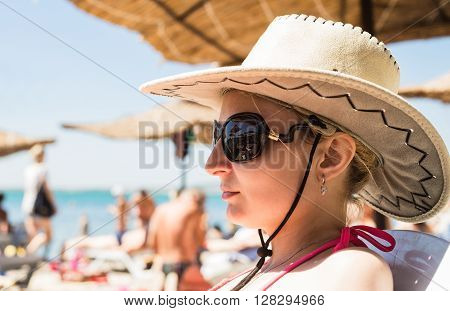 Girl in hat with large fields sunning on the beach near the sea