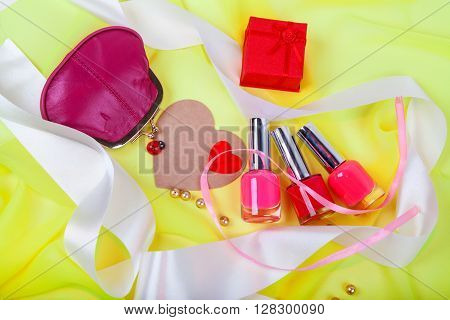 bottles of nail polish on a pink matter with white satin ribbons and female red purse