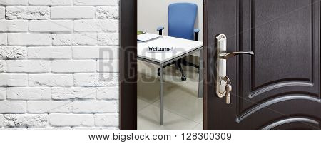 Welcome to the office. Half opened door to office. Door handle, door lock. Opening door. Privacy, safety concept. Entrance to the office workplace. Door at white brick wall, modern interior design.