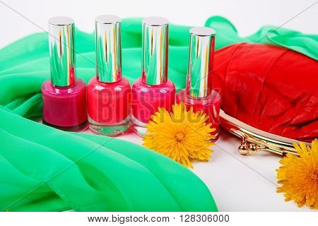Four red bottle with nail polish and red women's purse on a background of green tissue