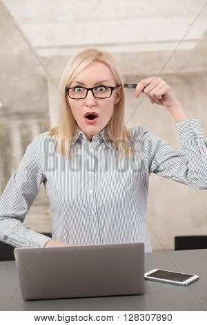 Shocked freelance lady holding flash card near her head showing about bad memory in office while working on laptop computer.