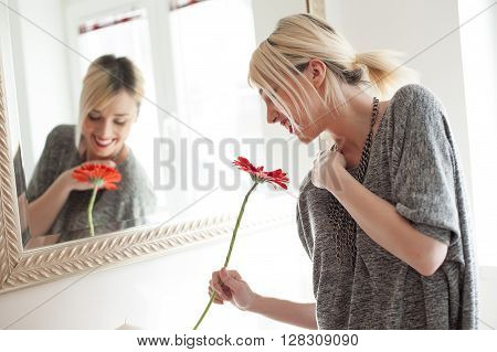 Fashion woman smelling gerbera flower near mirror