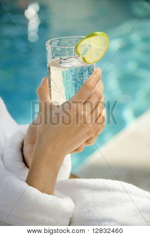 백인 여자의 손을 잡고 수영장 옆 라임 슬라이스 garnished 음료 유리.