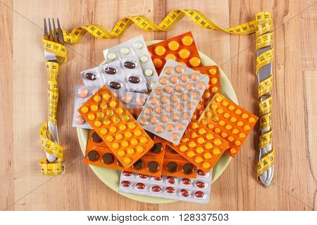 Fork and knife wrapped tape measure and blisters of medical pills capsules or supplements for therapy on plate concept of treatment health care slimming