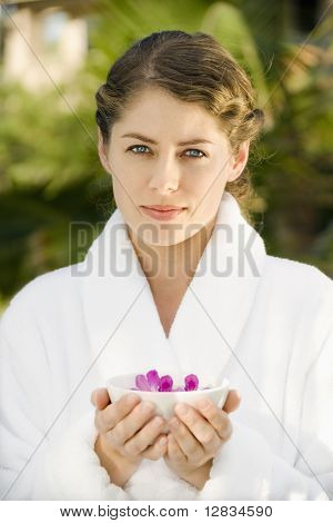 Attraktive kaukasischen adults in weißes Gewand hält Schüssel mit lila Orchideen, die im Wasser schweben.