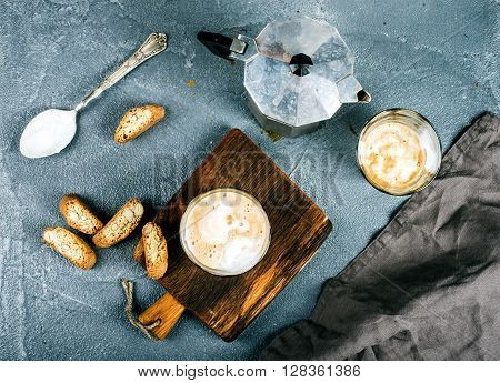 Glasses of coffee with ice cream on rustic wooden board, steel Italian Moka pot over grey concrete textured background, top view