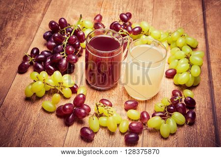 Glass of red stum and 2 glasses of white stum together with some green and red grapes photpgraphed on a piece of wood in retro style.