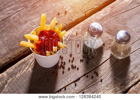 Fries and salt with pepperbox. Pepperbox and cup of fries. Spicy snack on aged table. Taste the energy.