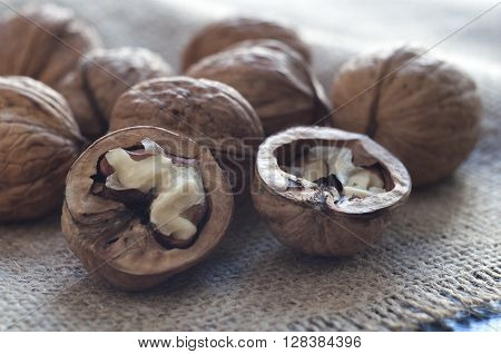 Opened walnut in the foreground. Close-up. Near several walnuts. Burlap on a table of black wood. Horizontal shot.