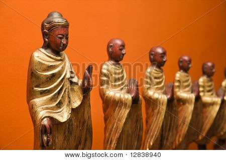 Fából készült szobrok Buddha tanítványai narancssárga falnak.