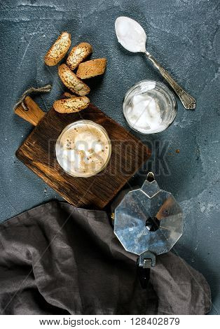Glasses of coffee with ice cream on rustic wooden board, steel Italian Moka pot over grey concrete textured background, top view, vertical